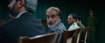 Movie still from “Holy Spider” (2022), directed by Ali Abbasi – An older man sitting in front of other men; Close Up shot, Over the shoulder angle