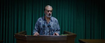 Movie still from “Holy Spider” (2022), directed by Ali Abbasi – An older man standing at a podium with microphones in front of him; Medium shot, Low angle