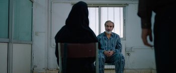 Movie still from “Holy Spider” (2022), directed by Ali Abbasi – An older man sitting in front of an older woman; Medium shot, Over the shoulder angle