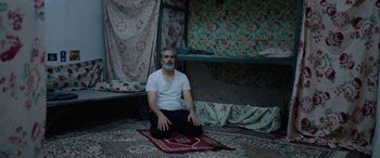 Movie still from “Holy Spider” (2022), directed by Ali Abbasi – A man sitting on the ground in a room; Wide shot, High angle