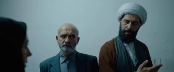 Movie still from “Holy Spider” (2022), directed by Ali Abbasi – Two men standing next to each other in front of a white wall; Medium shot, Low angle