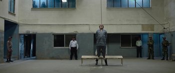 Movie still from “Holy Spider” (2022), directed by Ali Abbasi – A man standing on top of a wooden bench; Wide shot, Low angle