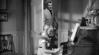 Movie still from “The Bad Seed” (1956), directed by Mervyn LeRoy – A young girl and an older man playing a piano together; Medium shot, Over the shoulder angle