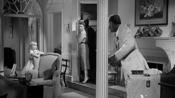 Movie still from “The Bad Seed” (1956), directed by Mervyn LeRoy – A man and a woman are standing in a living room; Wide shot, Over the shoulder angle