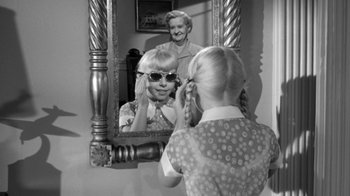 Movie still from “The Bad Seed” (1956), directed by Mervyn LeRoy – A young girl looking in the mirror while wearing sunglasses; Medium shot, Over the shoulder angle