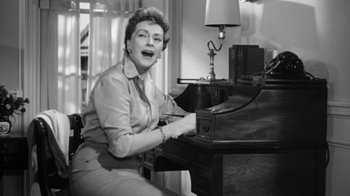 Movie still from “The Bad Seed” (1956), directed by Mervyn LeRoy – An older woman sitting at a desk playing a piano; Medium shot, Low angle