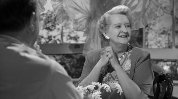 Movie still from “The Bad Seed” (1956), directed by Mervyn LeRoy – An older woman smiles while holding her hands; Close Up shot, Over the shoulder angle
