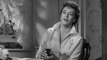 Movie still from “The Bad Seed” (1956), directed by Mervyn LeRoy – A woman sitting at a table holding a glass of wine; Close Up shot, Low angle