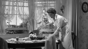 Movie still from “The Bad Seed” (1956), directed by Mervyn LeRoy – An old black and white photo of a woman setting a table; Medium shot, High angle