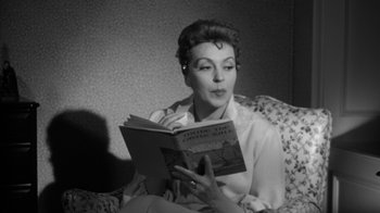 Movie still from “The Bad Seed” (1956), directed by Mervyn LeRoy – A black and white photo of a woman reading a book; Close Up shot, Low angle