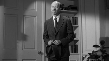 Movie still from “The Bad Seed” (1956), directed by Mervyn LeRoy – A black and white photo of a man in a suit and tie holding a hat; Medium shot, Low angle