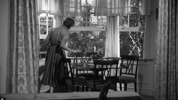 Movie still from “The Bad Seed” (1956), directed by Mervyn LeRoy – An old photo of a woman setting a dining room table; Wide shot, Low angle