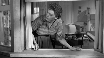 Movie still from “The Bad Seed” (1956), directed by Mervyn LeRoy – An old black and white photo of a woman cutting a piece of paper; Medium shot, Low angle