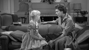 Movie still from “The Bad Seed” (1956), directed by Mervyn LeRoy – An old photo of a man and a little girl sitting on a couch; Medium shot, Over the shoulder angle