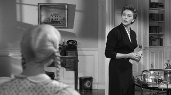 Movie still from “The Bad Seed” (1956), directed by Mervyn LeRoy – A woman standing in front of another woman in front of a mirror; Medium shot, Over the shoulder angle