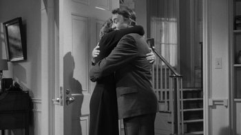 Movie still from “The Bad Seed” (1956), directed by Mervyn LeRoy – A man and a woman hugging in front of a door; Medium shot, High angle