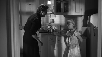 Movie still from “The Bad Seed” (1956), directed by Mervyn LeRoy – An old photo of a woman and a little girl in a kitchen; Medium shot, Over the shoulder angle