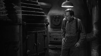 Movie still from “The Bad Seed” (1956), directed by Mervyn LeRoy – A black and white photo of a man standing in front of an oven; Medium shot, High angle