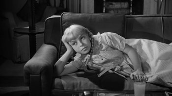 Movie still from “The Bad Seed” (1956), directed by Mervyn LeRoy – A young girl sitting on a couch with her head resting on the arm of the chair; Medium shot, High angle