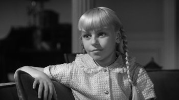 Movie still from “The Bad Seed” (1956), directed by Mervyn LeRoy – A young girl sitting in a chair with her hands on her chin; Close Up shot, Over the shoulder angle