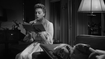 Movie still from “The Bad Seed” (1956), directed by Mervyn LeRoy – A woman sitting on a couch reading a book to a sleeping girl; Medium shot, Low angle