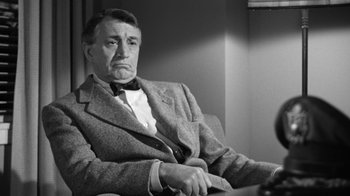 Movie still from “The Bad Seed” (1956), directed by Mervyn LeRoy – An older man sitting in a chair wearing a suit and bow tie; Close Up shot, Over the shoulder angle