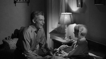 Movie still from “The Bad Seed” (1956), directed by Mervyn LeRoy – An old photo of a man and a woman sitting on a bed; Medium shot, Over the shoulder angle