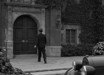 Movie still from “The Bad and the Beautiful” (1952), directed by Vincente Minnelli – A black and white photo of a man in a suit and a hat walking in front of a building; Wide shot, High angle