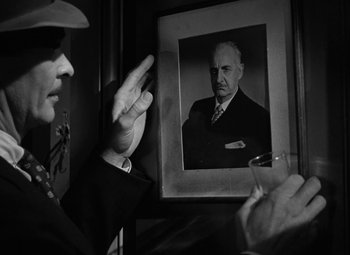 Movie still from “The Bad and the Beautiful” (1952), directed by Vincente Minnelli – A black and white photo of a man holding his hand up in front of a picture of a man; Close Up shot, Low angle
