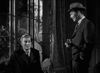 Movie still from “The Bad and the Beautiful” (1952), directed by Vincente Minnelli – Two men in suits and a hat are talking to each other; Medium shot, Over the shoulder angle