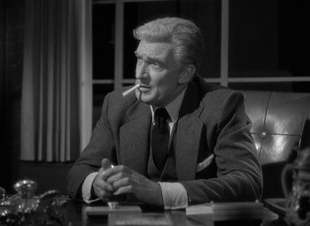 Movie still from “The Bad and the Beautiful” (1952), directed by Vincente Minnelli – An older man sitting at a table with a cigarette in his mouth; Medium shot, High angle