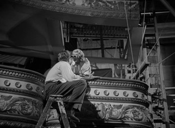 Movie still from “The Bad and the Beautiful” (1952), directed by Vincente Minnelli – Two people are sitting on a ladder in front of a building; Wide shot, Low angle