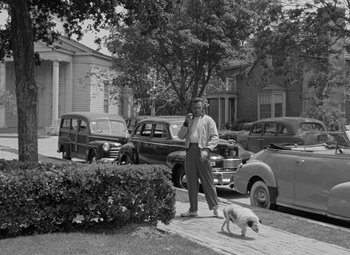 Movie still from “The Bad and the Beautiful” (1952), directed by Vincente Minnelli – A black and white photo of a man and a dog on the sidewalk; Wide shot, Low angle