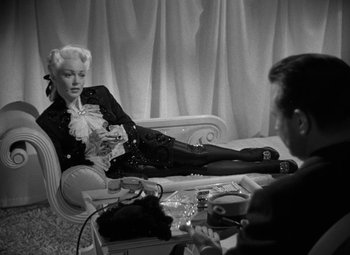 Movie still from “The Bad and the Beautiful” (1952), directed by Vincente Minnelli – A woman sitting on top of a couch next to a man; Medium shot, Over the shoulder angle