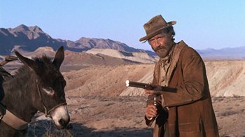 Movie still from “The Ballad of Cable Hogue” (1970), directed by Sam Peckinpah – A man in a hat standing next to a donkey; Medium shot, Low angle