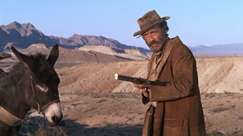 Movie still from “The Ballad of Cable Hogue” (1970), directed by Sam Peckinpah – A man holding a gun while standing next to a horse; Medium shot, Low angle