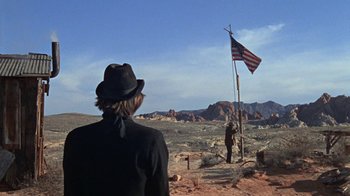 Movie still from “The Ballad of Cable Hogue” (1970), directed by Sam Peckinpah – A man standing next to an american flag on top of a pole; Wide shot, Low angle