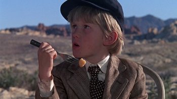 Movie still from “The Ballad of Cable Hogue” (1970), directed by Sam Peckinpah – A young boy in a suit and tie holding a fork in his mouth; Close Up shot, Low angle