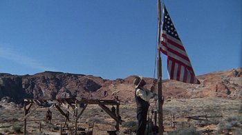 Movie still from “The Ballad of Cable Hogue” (1970), directed by Sam Peckinpah – A man standing next to an american flag on top of a pole; Wide shot, Low angle