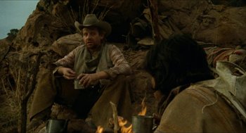 Movie still from “The Ballad of Gregorio Cortez” (1982), directed by Robert M. Young – A man sitting on the ground next to a fire pit; Medium shot, Over the shoulder angle