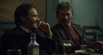Movie still from “The Ballad of Gregorio Cortez” (1982), directed by Robert M. Young – Two men sitting at a table with a bottle of beer; Medium shot, Over the shoulder angle