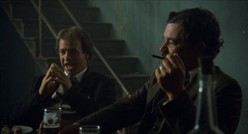 Movie still from “The Ballad of Gregorio Cortez” (1982), directed by Robert M. Young – Two men are sitting at a table and one is smoking a cigarette; Medium shot, Low angle