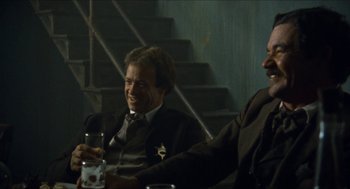 Movie still from “The Ballad of Gregorio Cortez” (1982), directed by Robert M. Young – Two men in suits sitting at a table with drinks; Medium shot, Low angle