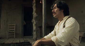 Movie still from “The Ballad of Gregorio Cortez” (1982), directed by Robert M. Young – A man sitting on a bench in front of a building; Medium shot, Low angle