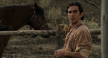 Movie still from “The Ballad of Gregorio Cortez” (1982), directed by Robert M. Young – A man standing next to a horse in a fenced in area; Medium shot, Low angle