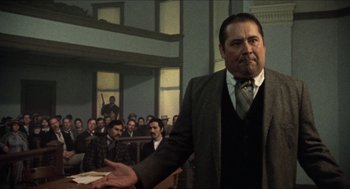 Movie still from “The Ballad of Gregorio Cortez” (1982), directed by Robert M. Young – A man in a suit and tie in front of a group of people; Medium shot, Low angle