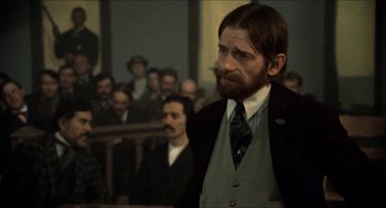 Movie still from “The Ballad of Gregorio Cortez” (1982), directed by Robert M. Young – A man in a suit and tie in front of a group of people; Medium shot, Over the shoulder angle