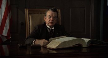 Movie still from “The Ballad of Gregorio Cortez” (1982), directed by Robert M. Young – An older man sitting at a table with papers in front of him; Medium shot, Low angle