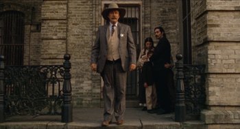 Movie still from “The Ballad of Gregorio Cortez” (1982), directed by Robert M. Young – An older man in a suit and hat standing on a sidewalk; Wide shot, Low angle
