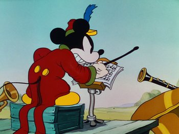 Movie still from “The Band Concert” (1935), directed by Wilfred Jackson – A mickey mouse cartoon character sitting in front of an easel; Wide shot, Low angle